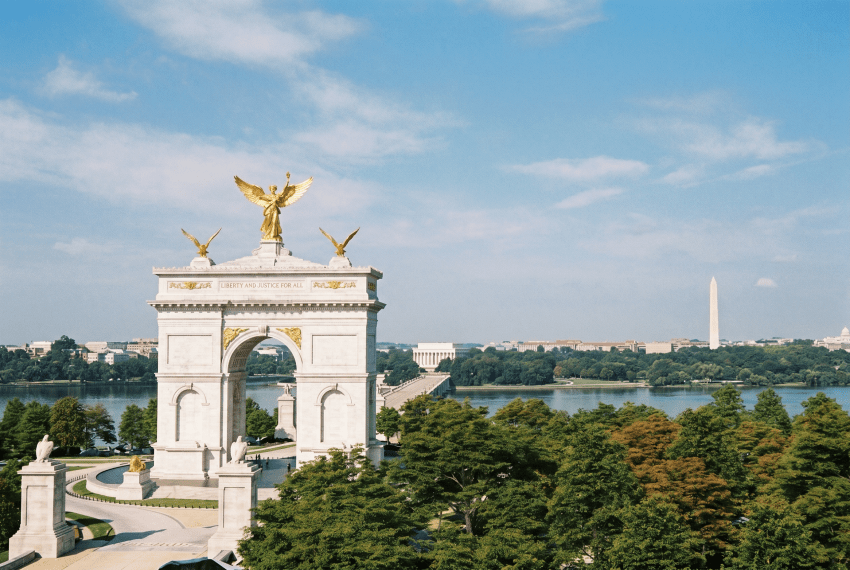 AI-rendered aerial photo of a white triumphal arch with gold statues overlooking the Potomac River, Lincoln Memorial, and Washington Monument in the distance.