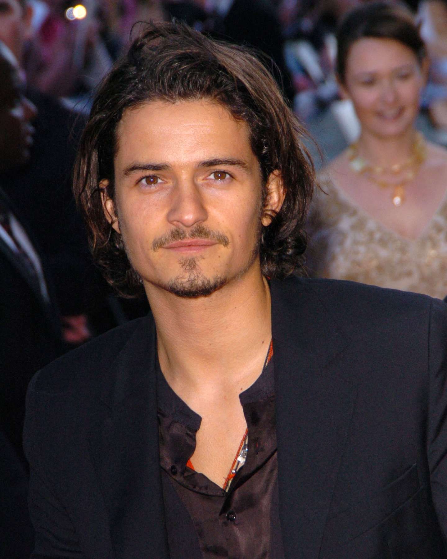 Click to open the image gallery Dark-haired man with medium-length hair and a goatee in a black blazer looks toward the camera at a red carpet premiere.