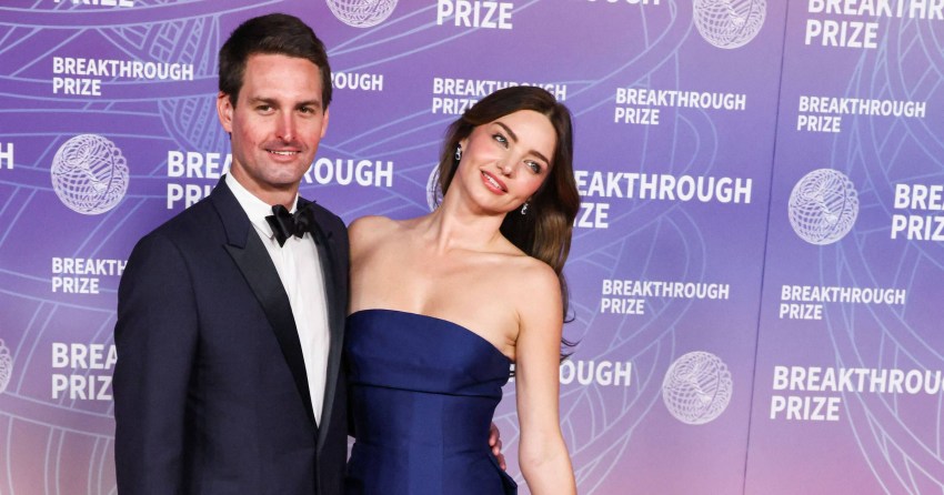 Miranda Kerr in a strapless navy blue ball gown and Evan Spiegel in a dark suit posing together at the Breakthrough Prize Ceremony red carpet.