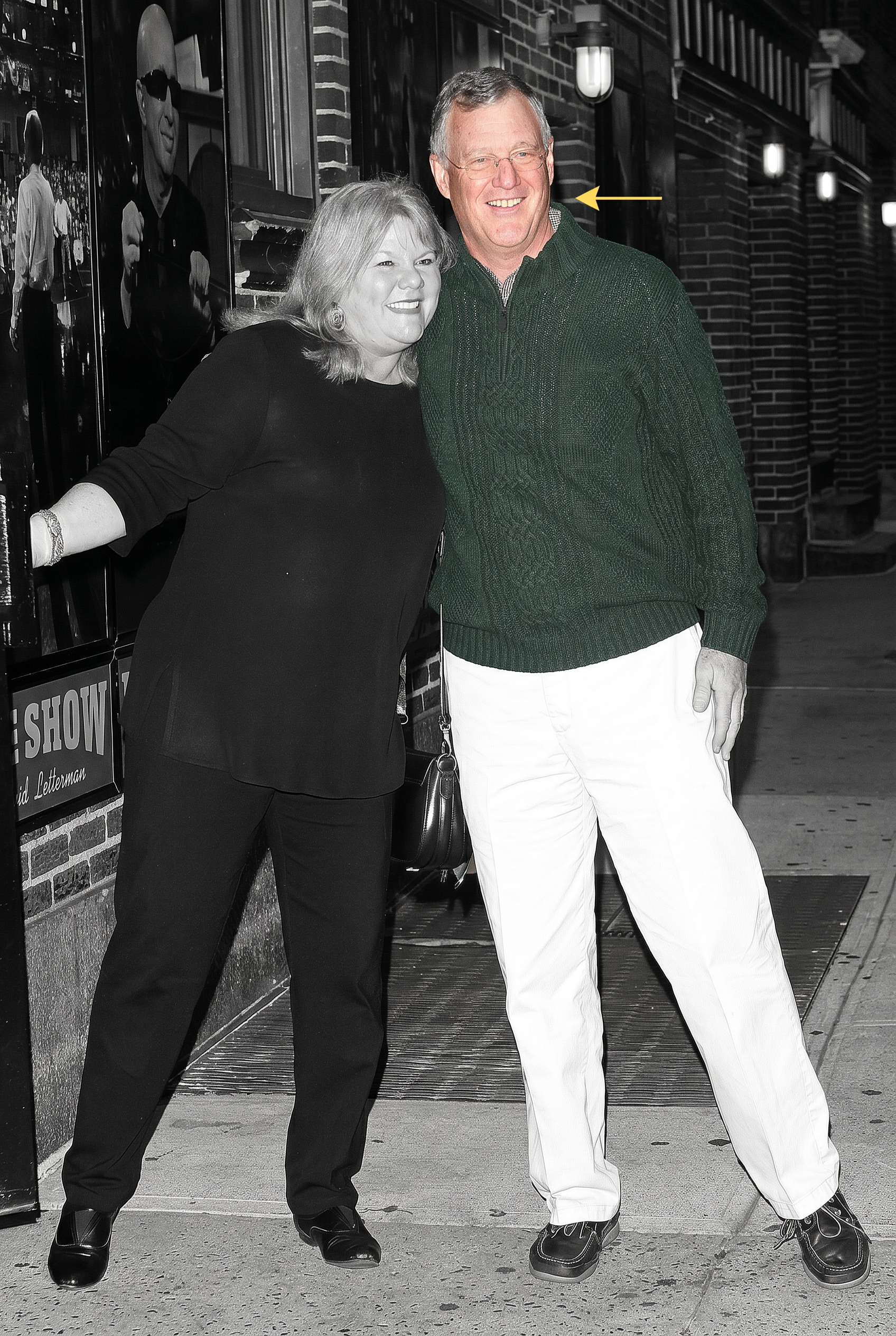 Click to open the image gallery A man in a green sweater and white pants and a woman in all black smile together outside the Late Show with David Letterman, in a black-and-white photo with the man's sweater colorized green.