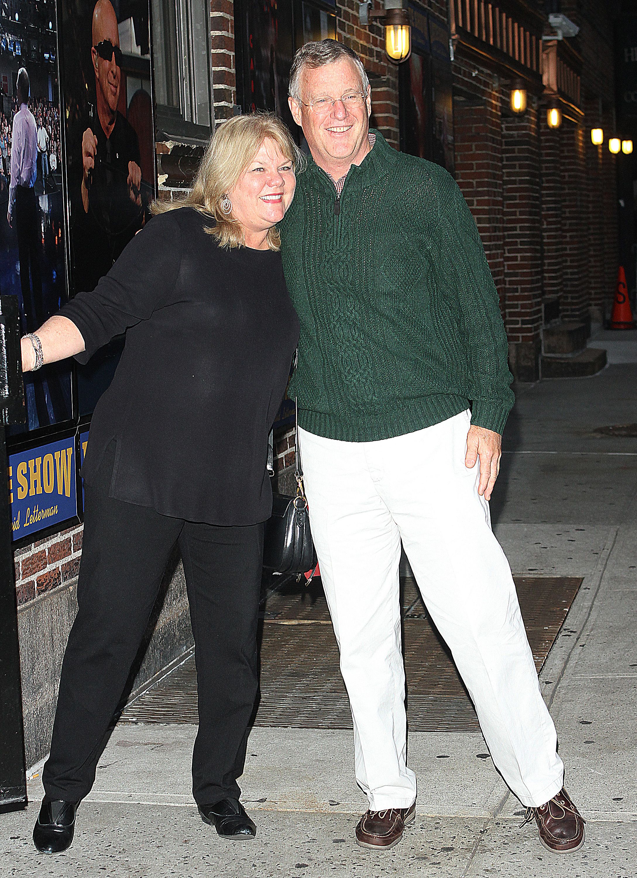 Click to open the image gallery A smiling couple — a woman in black and a tall man in a green cable-knit sweater and white pants — pose together on a sidewalk outside the Late Show with David Letterman.