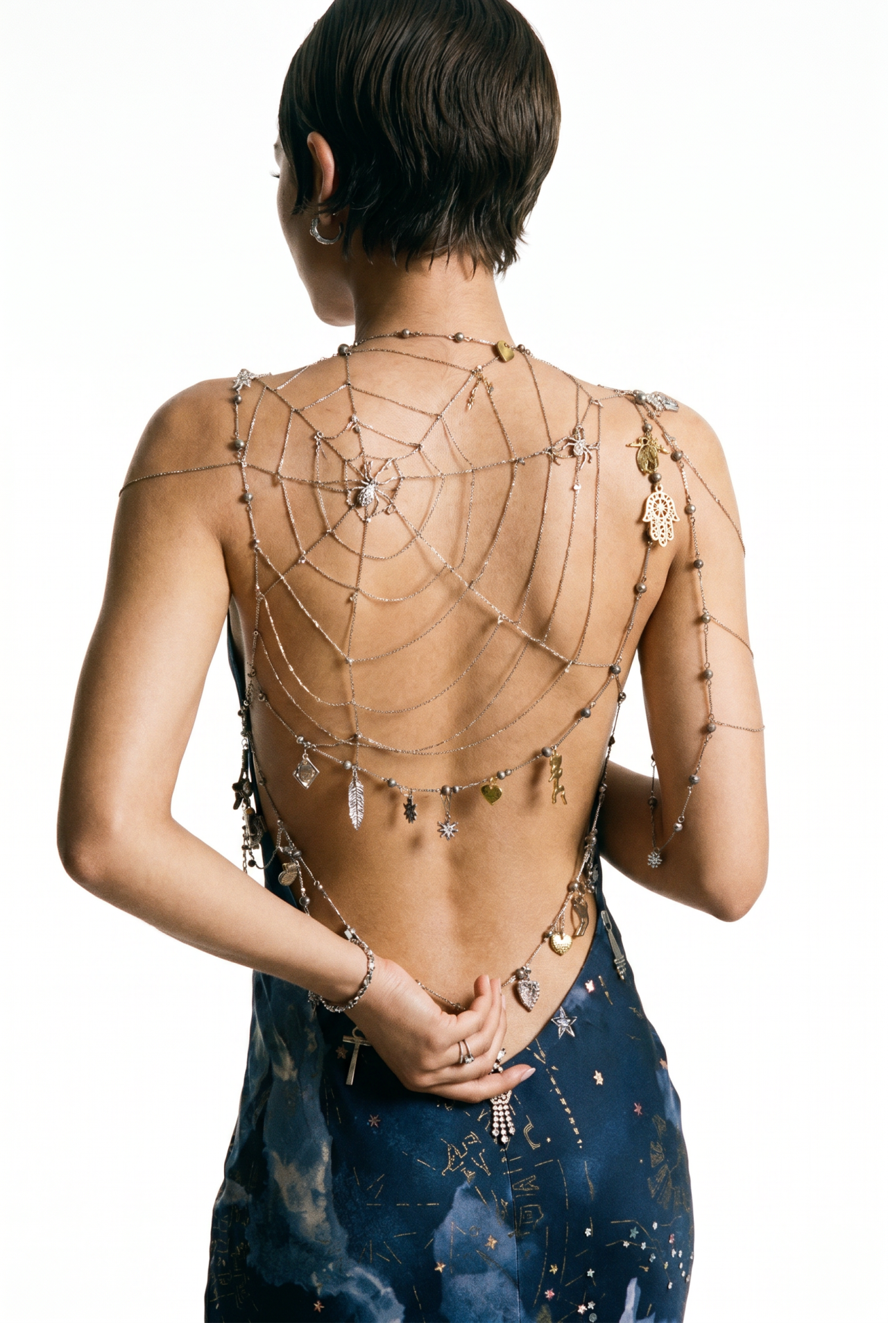 Woman in a backless blue gown with ornate silver spider-web chain body jewelry draping across her bare back at an outdoor event