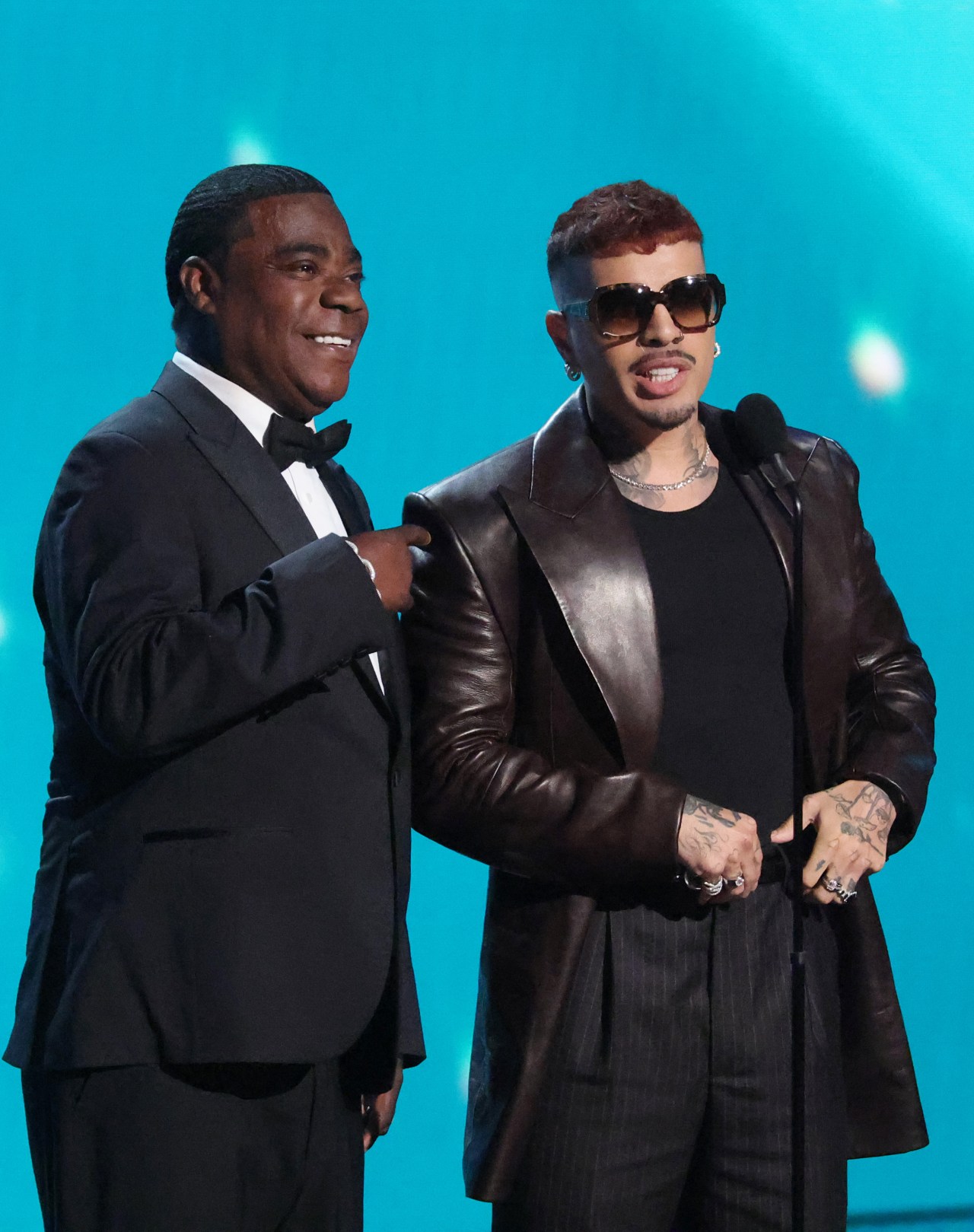 Tracy Morgan in a black tuxedo and Rauw Alejandro in a brown leather blazer and sunglasses presenting onstage at the 2026 ESPY Awards.
