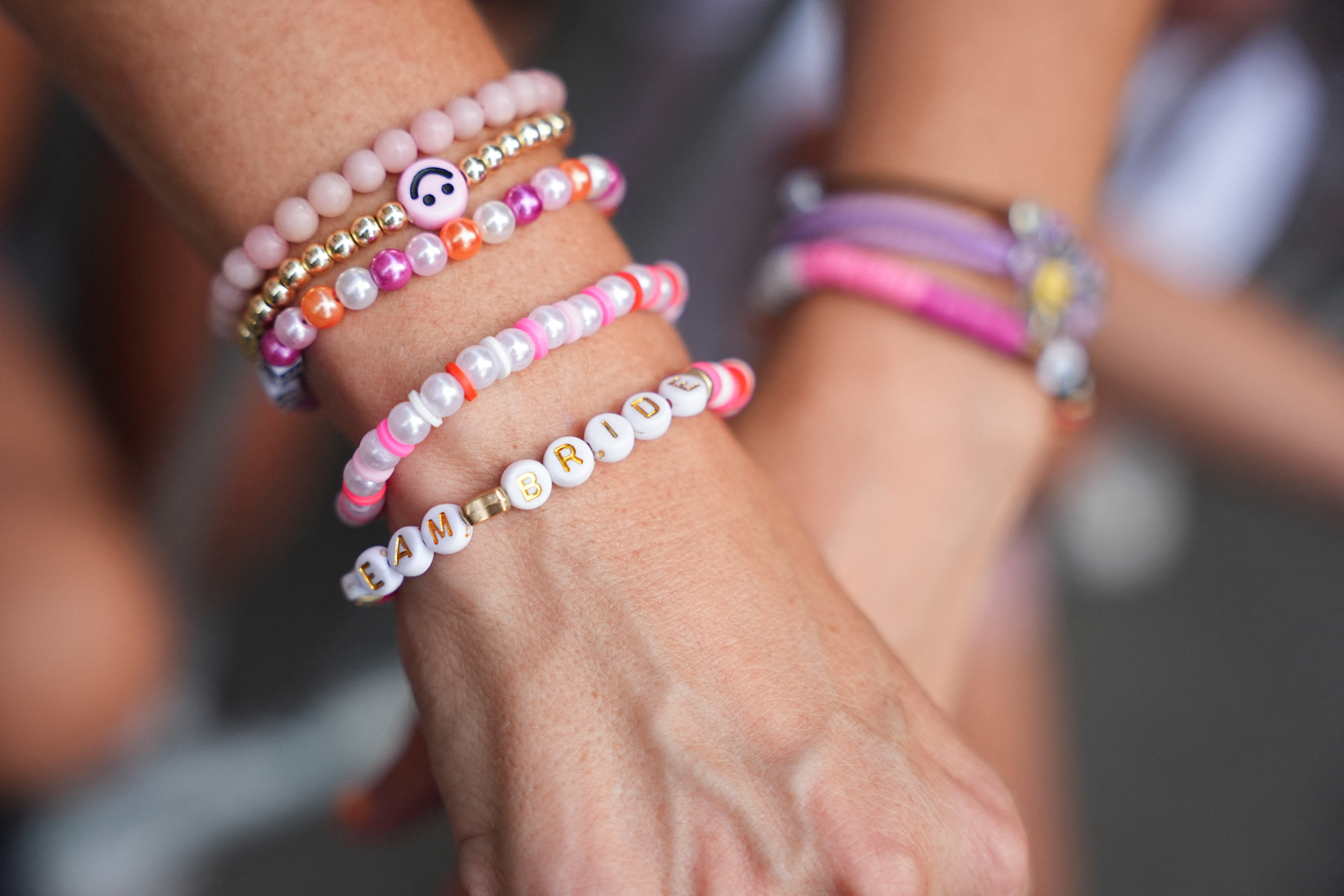 Close-up of a wrist stacked with colorful beaded bracelets, including one reading "Team Bride" in gold letters on white beads.