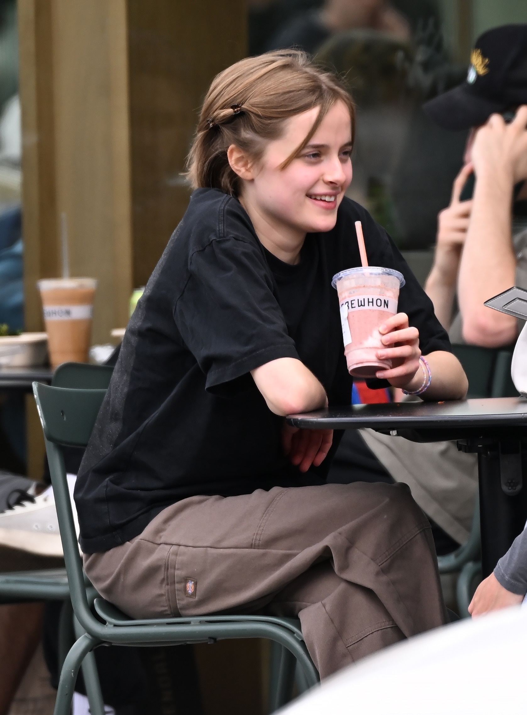 Click to open the image gallery Vivienne Jolie Pitt sitting outside Erewhon with a friend, holding a smoothie