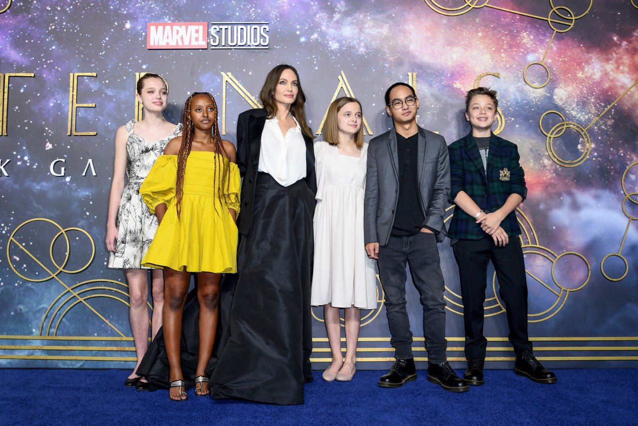 Angelina Jolie flanked by five of her children on the blue carpet at the UK premiere of Eternals, in front of a Marvel Studios backdrop.