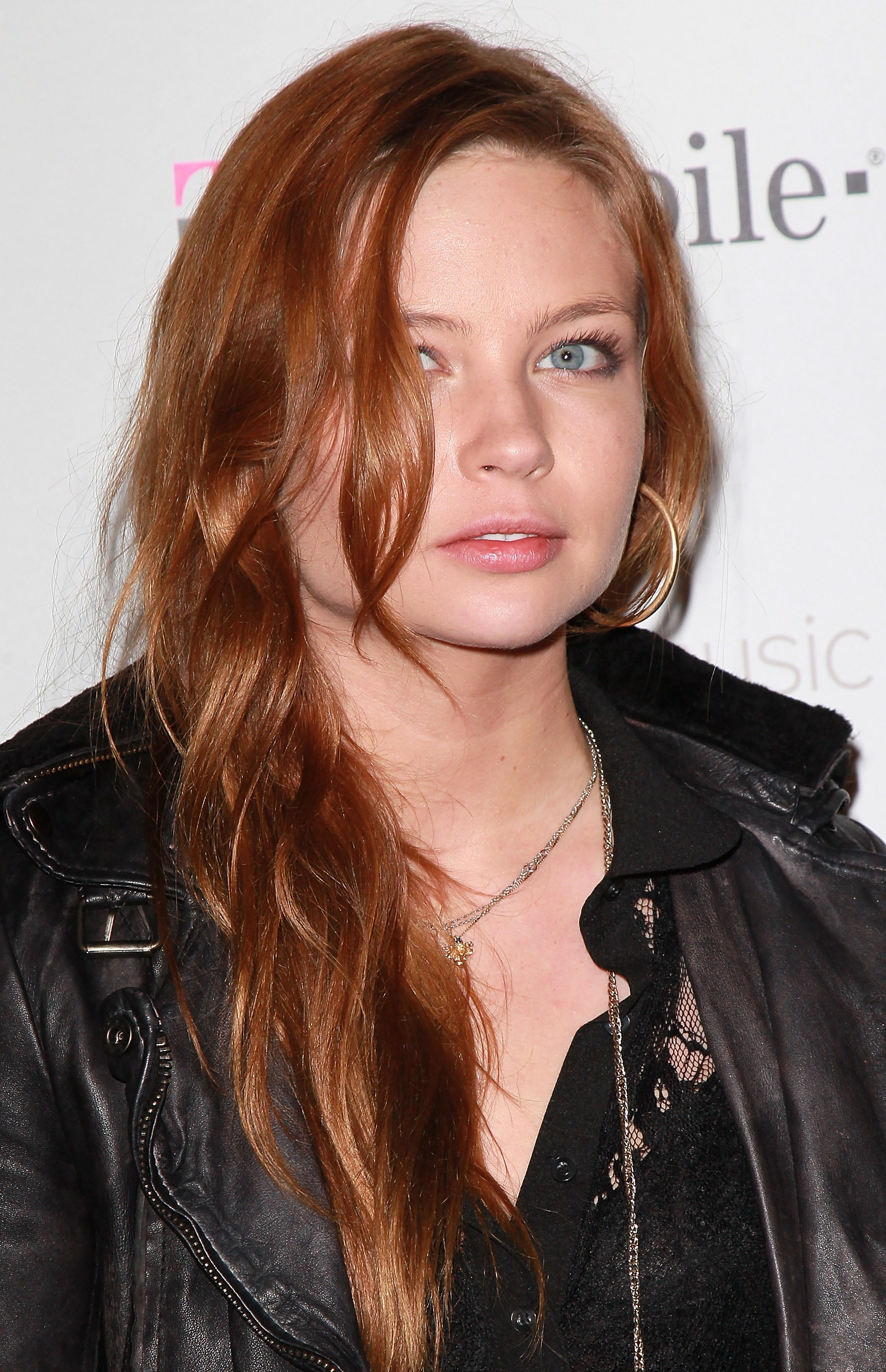 Click to open the image gallery Daveigh Chase with long auburn hair wearing a black leather jacket and lace top at a T-Mobile event backdrop.