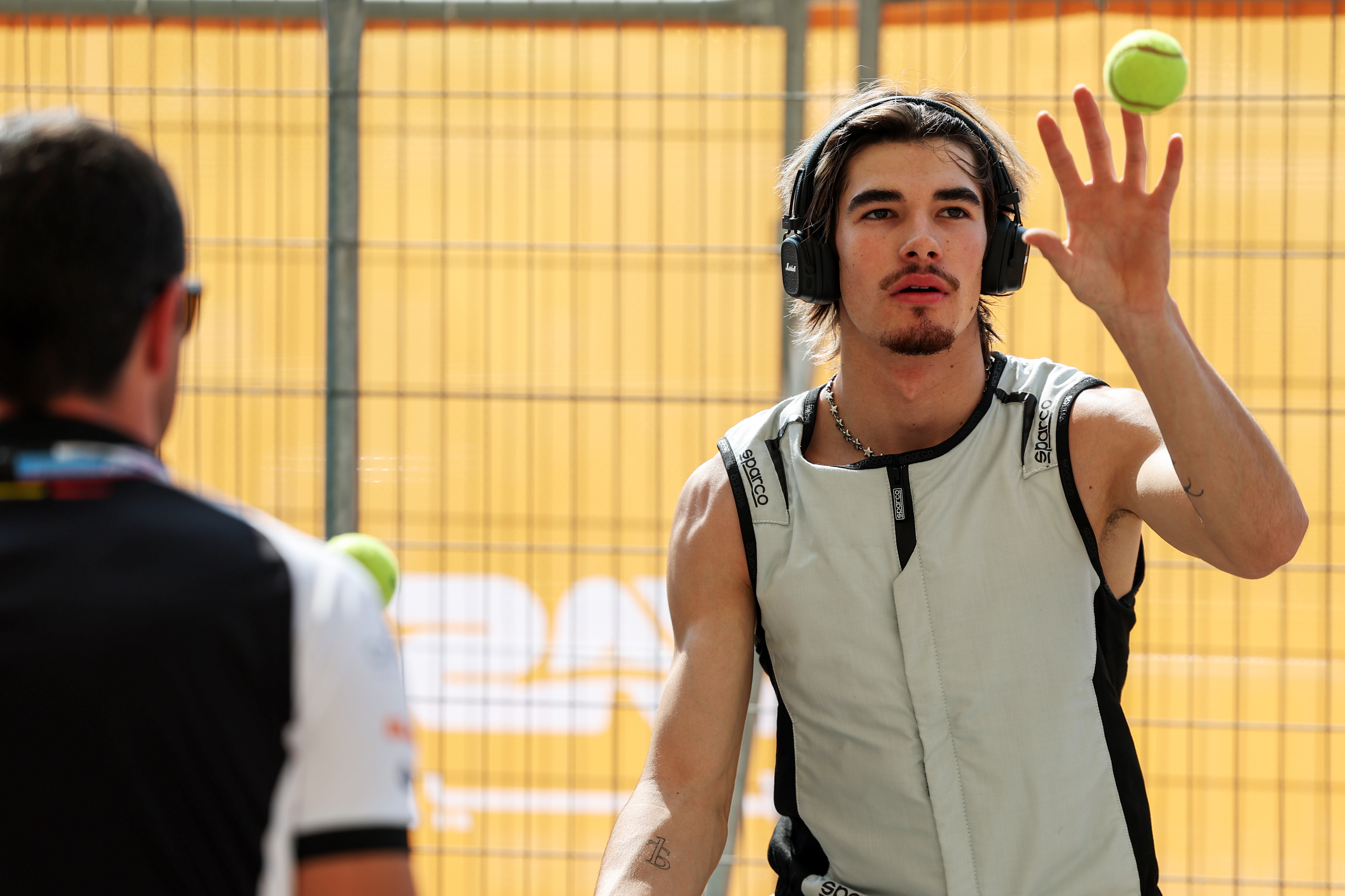 Nikola Tsolov in a Sparco vest and Marshall headphones tossing a tennis ball at the Abu Dhabi F2 round.