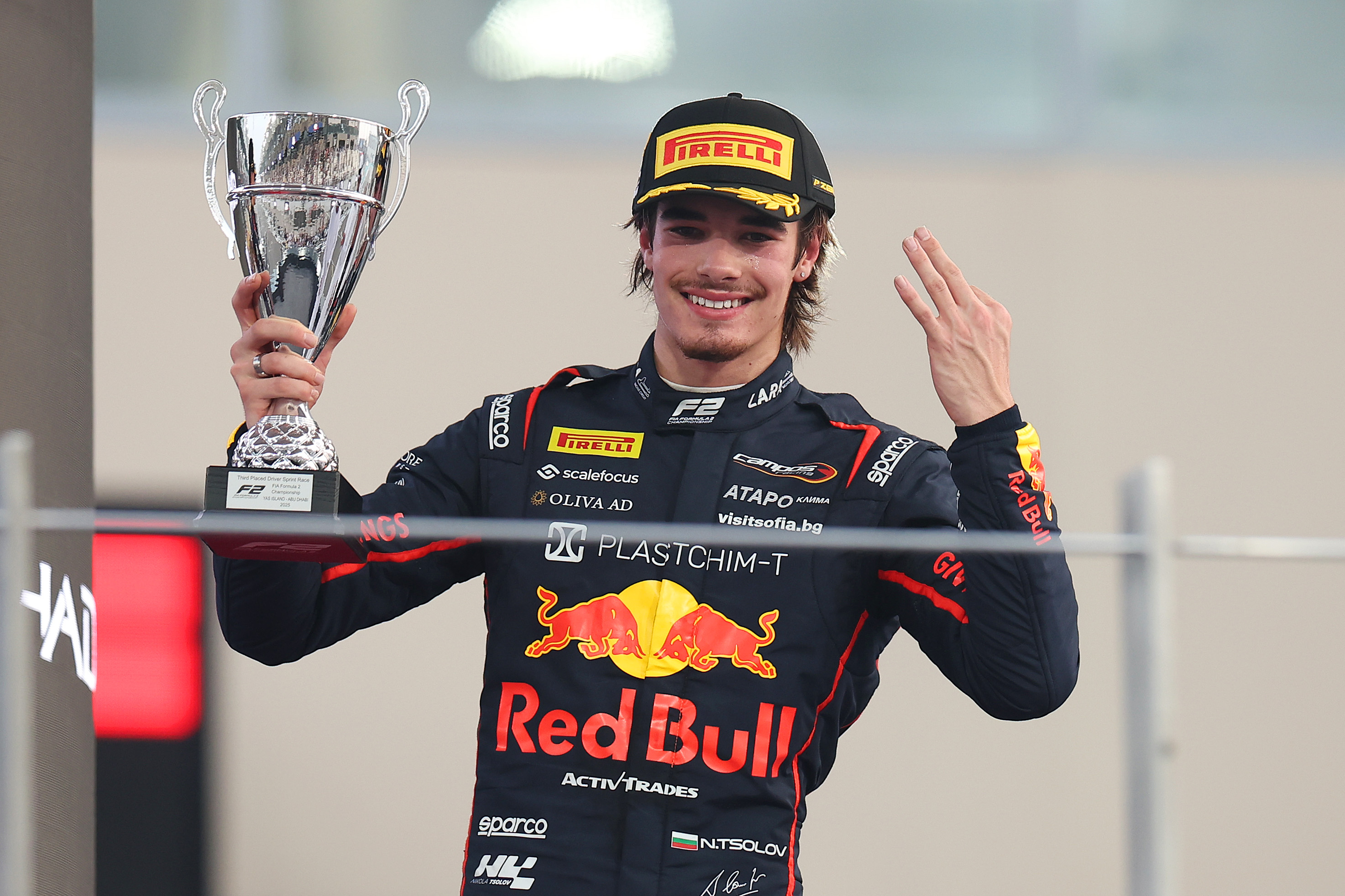 Nikola Tsolov holding a silver trophy on the podium in a Red Bull Campos Racing suit at Yas Marina Circuit.
