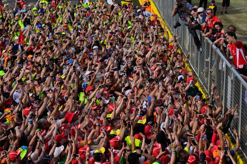 Massive crowd of Formula 1 fans with arms and phones raised on the Silverstone circuit after the British Grand Prix race.
