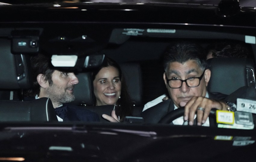 A man and a smiling woman seated in the back of a car at night, with a driver in the front seat wearing glasses.