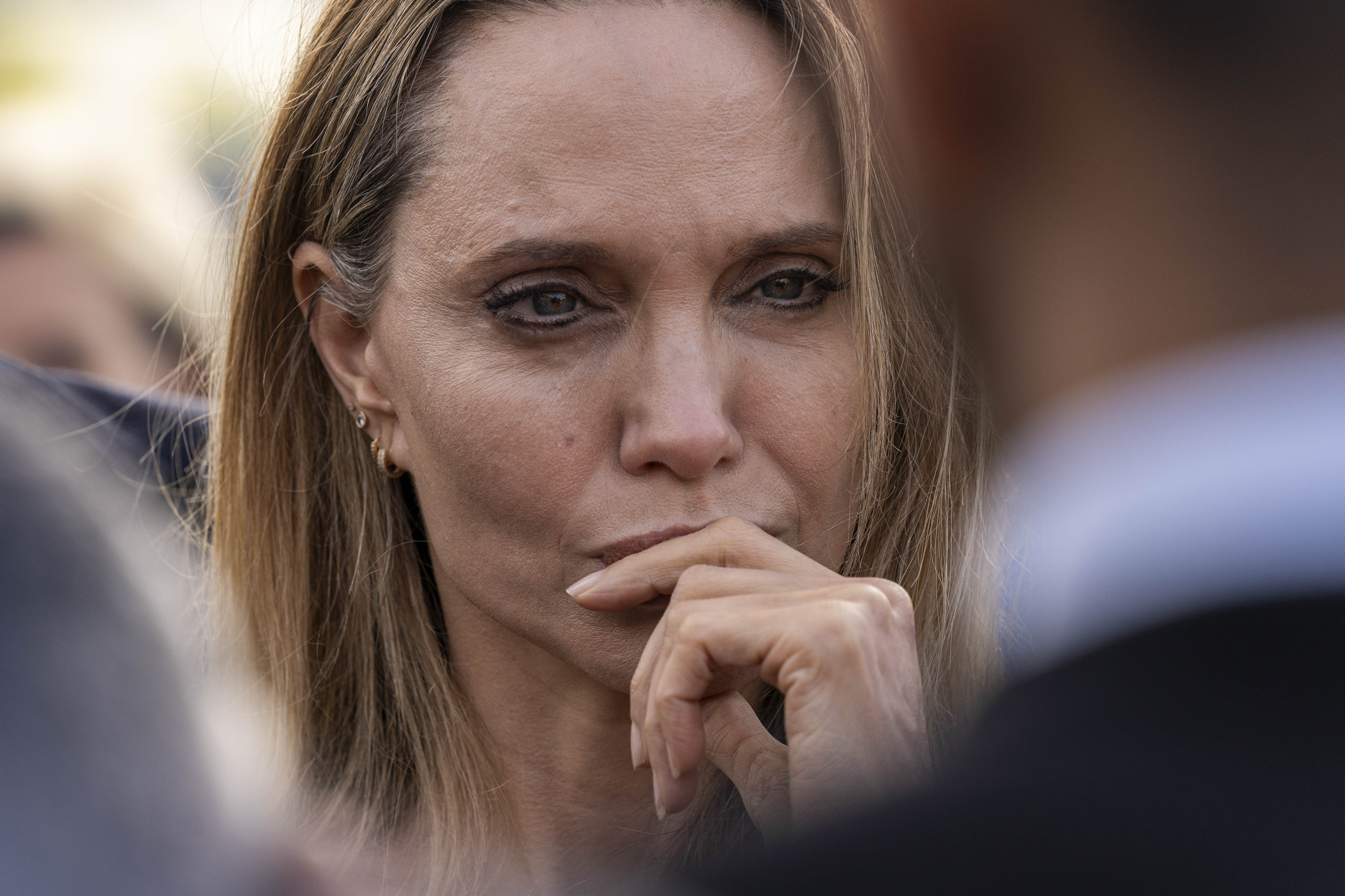 Tight close-up of a woman with straight blonde hair resting her fist against her lips, eyes focused intently ahead.
