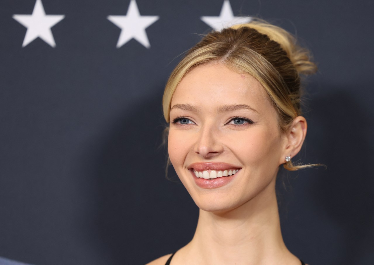 Apple Martin smiling at the New York premiere of Marty Supreme, with white stars on a dark blue backdrop behind her.