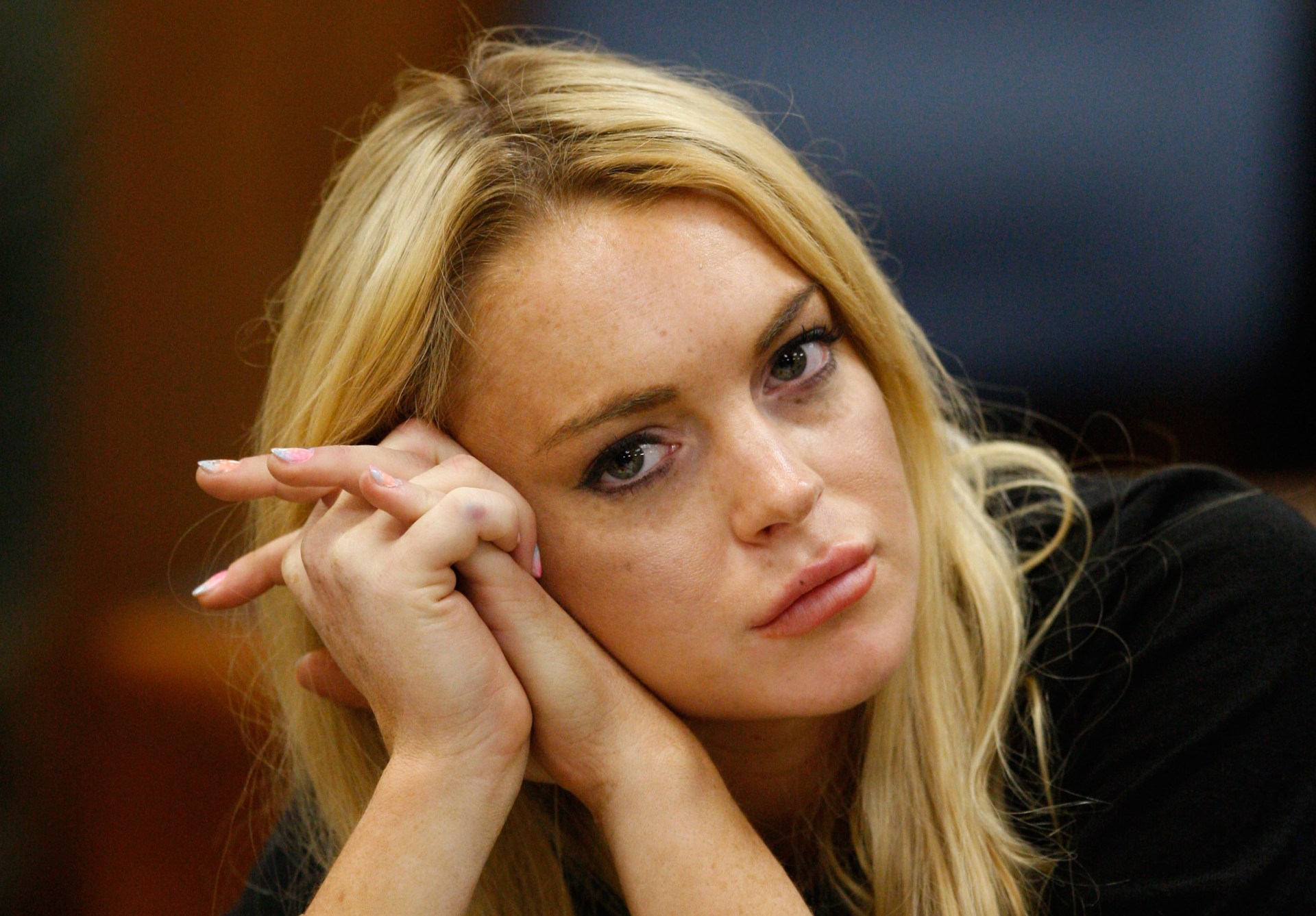 Blonde woman with hands clasped against her cheeks, looking toward the camera with a somber expression in a courtroom setting.