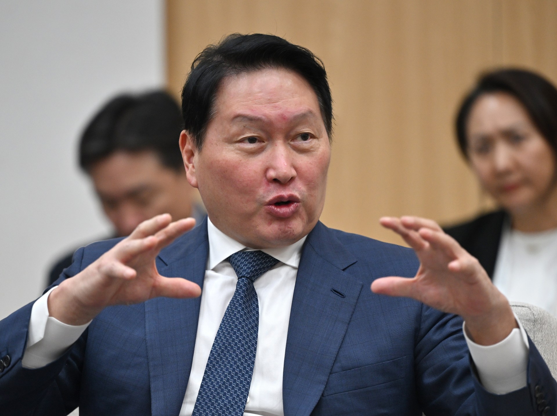SK Group Chairman Chey Tae-won in a blue suit and tie, speaking animatedly with both hands raised, at a meeting during the APEC summit in South Korea.