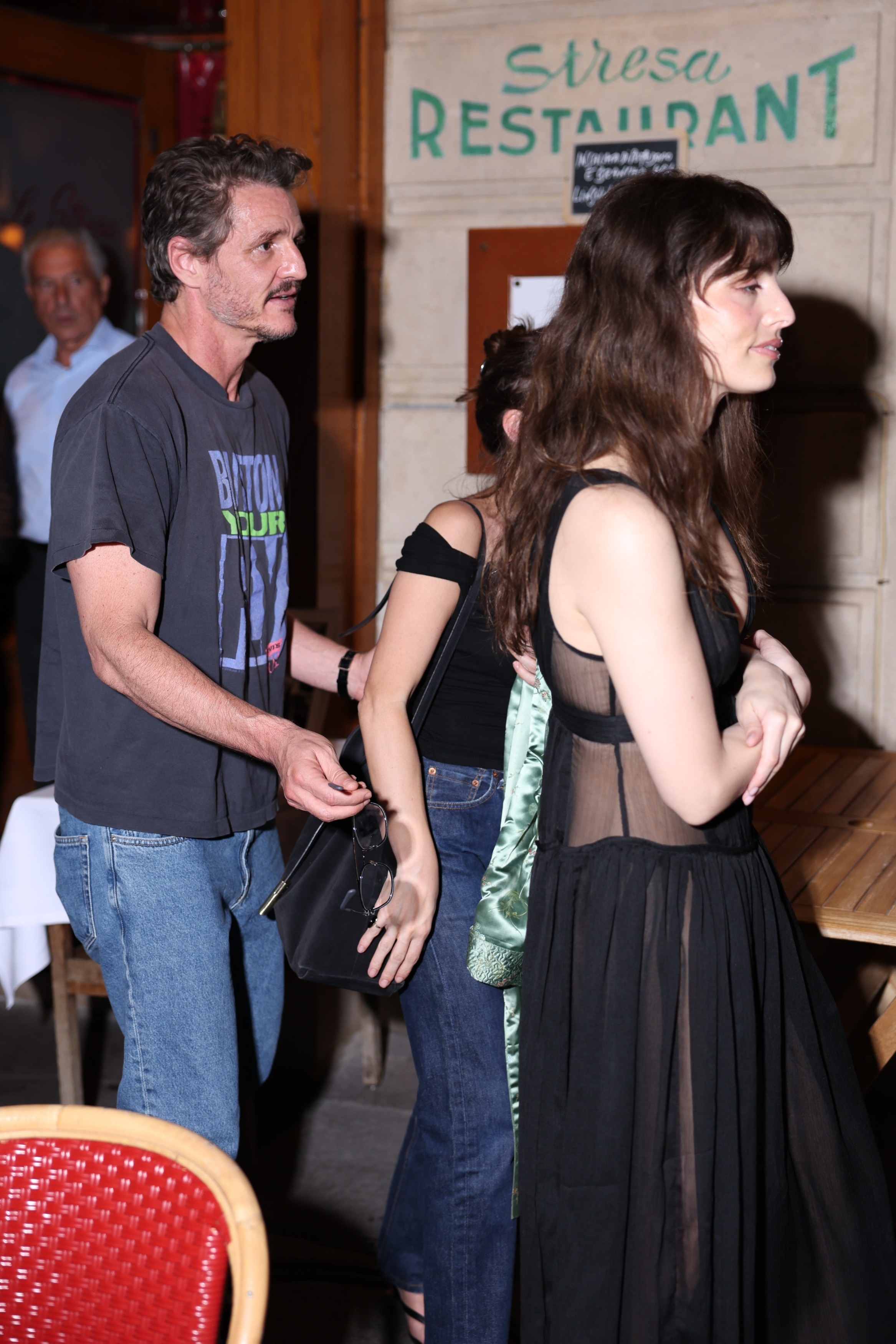 Man in dark graphic t-shirt and jeans standing next to a woman in a sheer black dress outside Stresa Restaurant in Paris.