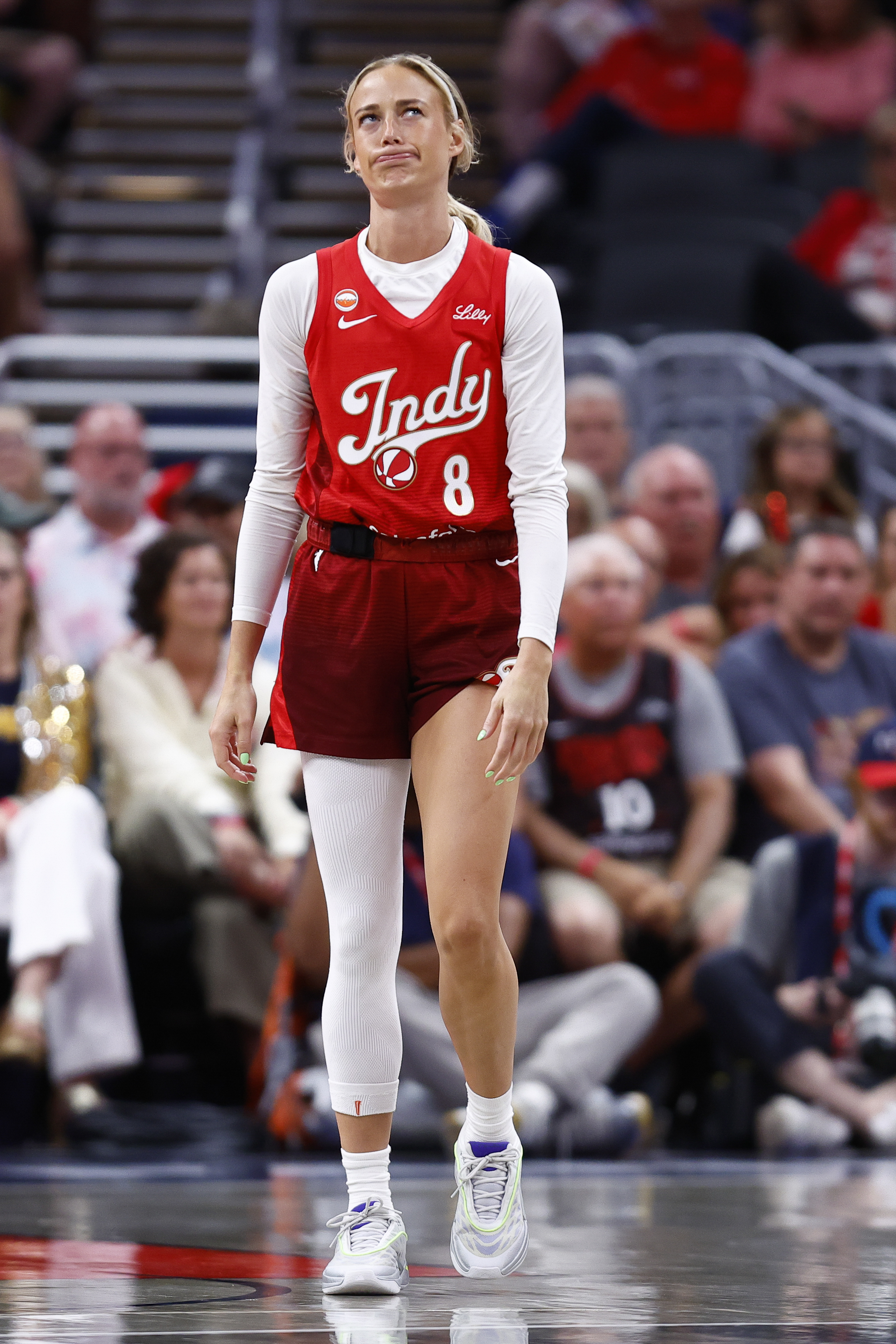 Indiana Fever guard Sophie Cunningham (#8) in a red Indy jersey looking up with a grimace during a WNBA game.