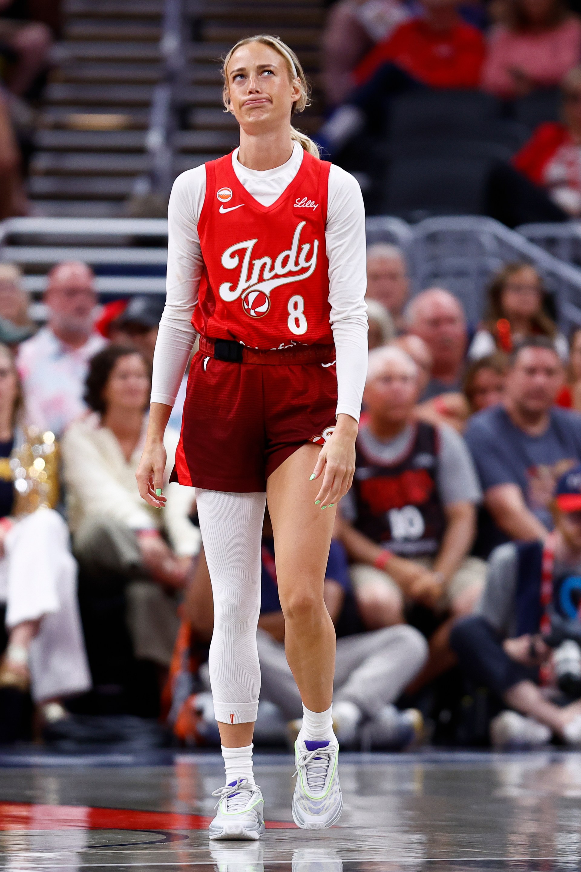Indiana Fever guard Sophie Cunningham (#8) in a red Indy jersey looking up with a grimace during a WNBA game.
