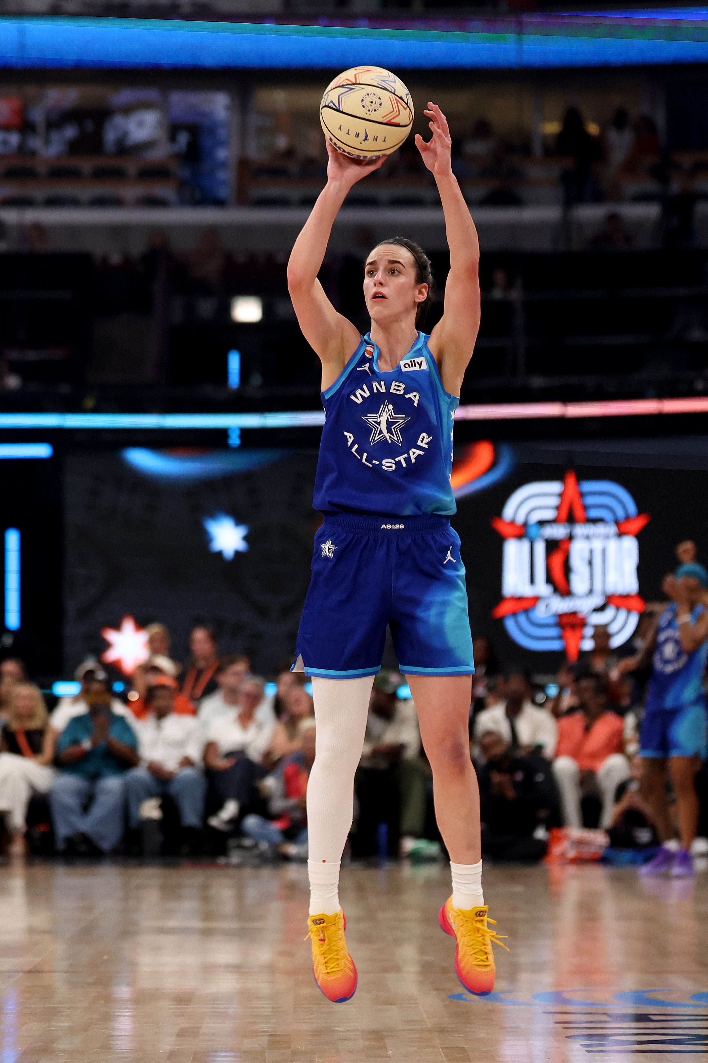 Caitlin Clark in a blue WNBA All-Star jersey jumping to shoot a basketball at the United Center in Chicago.