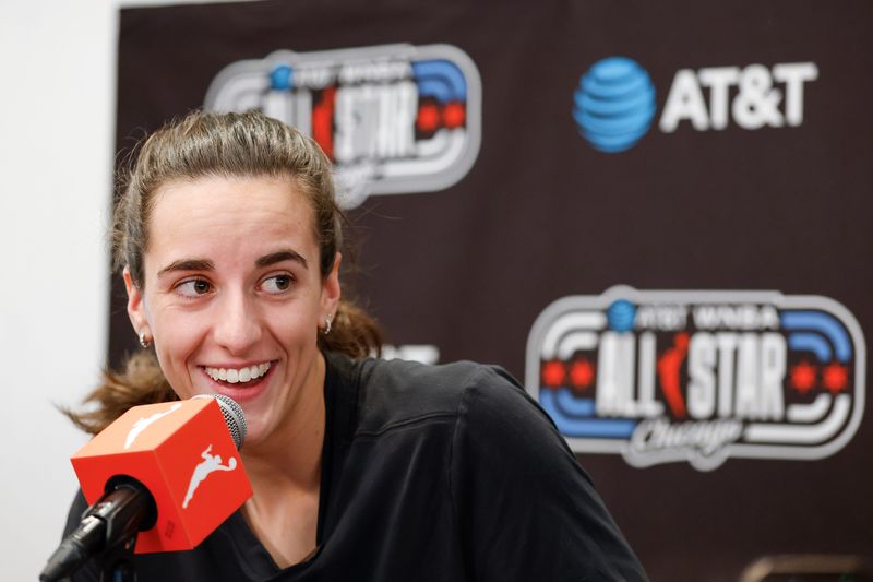 Caitlin Clark smiling and speaking into a WNBA-branded microphone at a press conference, with an AT&T WNBA All-Star Chicago backdrop behind her.