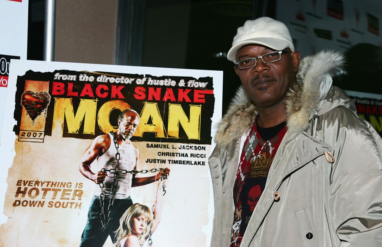Samuel L. Jackson in a white cap and fur-trimmed coat standing next to a Black Snake Moan movie poster at a premiere.