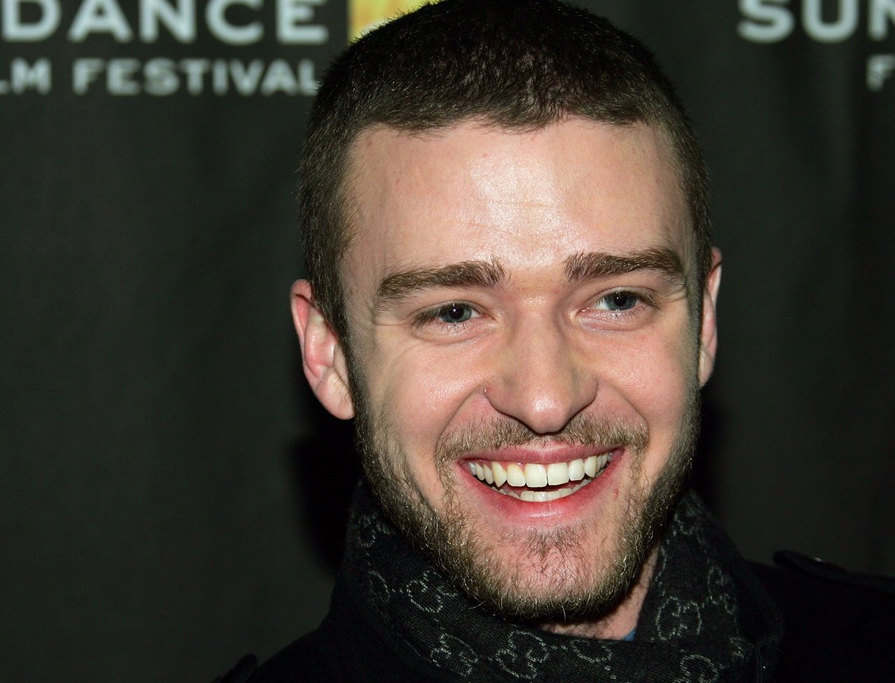 Close-up of a smiling young man with short hair and a beard, standing in front of a dark Sundance Film Festival backdrop.