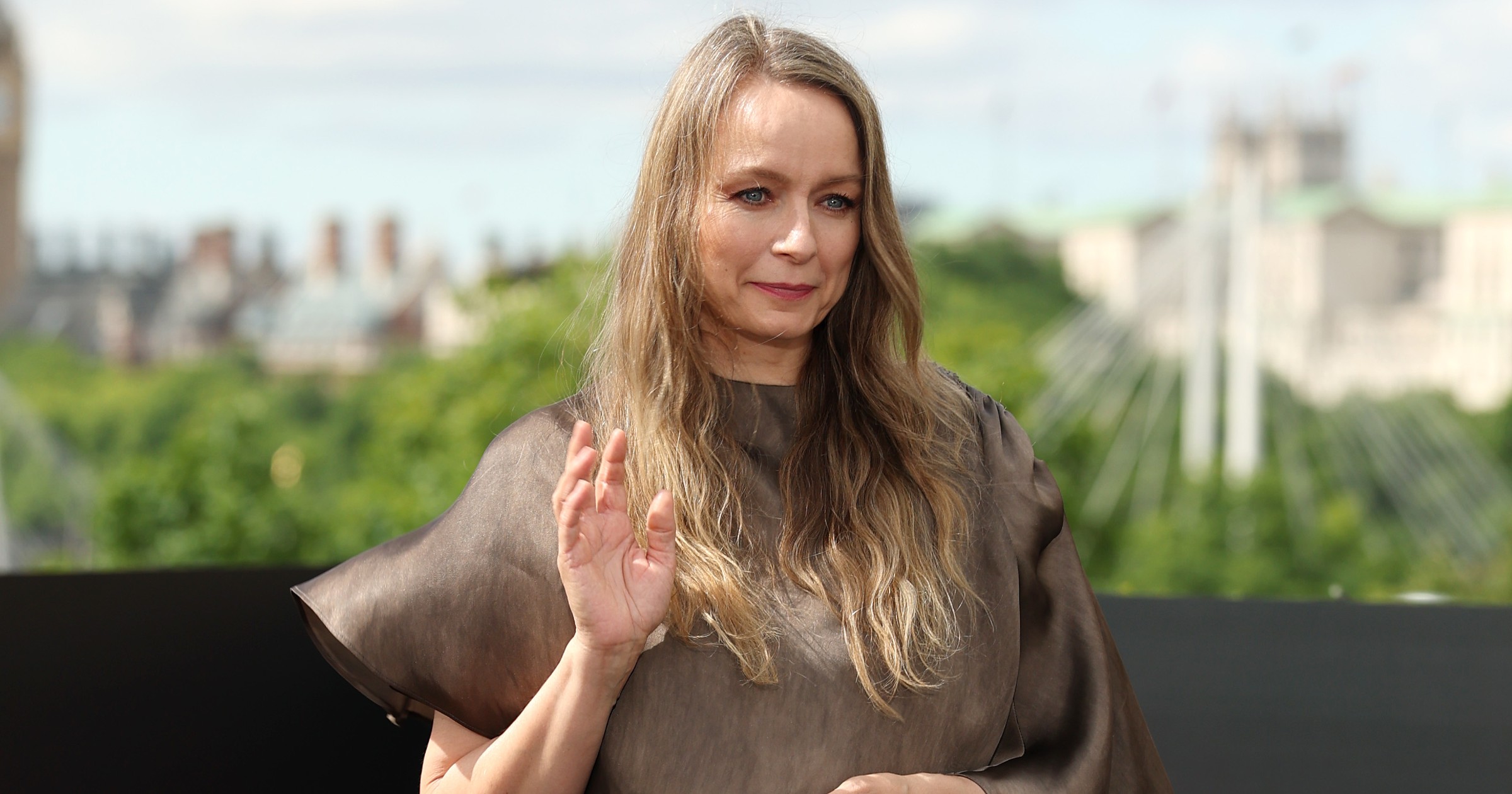 Samantha Morton in a flowing taupe satin gown, waving, at The Odyssey photocall in London with Big Ben in the background.