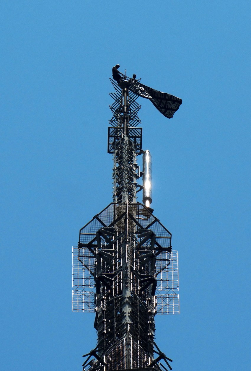 Two people displaying a banner during a protest on top of the Empire State Building in New York City