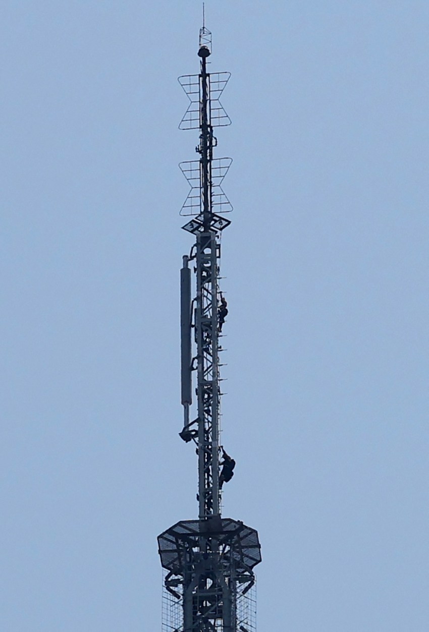 Two people on the spire of the Empire State Building holding an unfurled banner