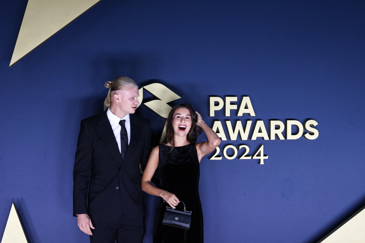 Erling Haaland looking sideways while Isabel Haugseng Johansen laughs and touches her hair in front of the PFA Awards 2024 sign.