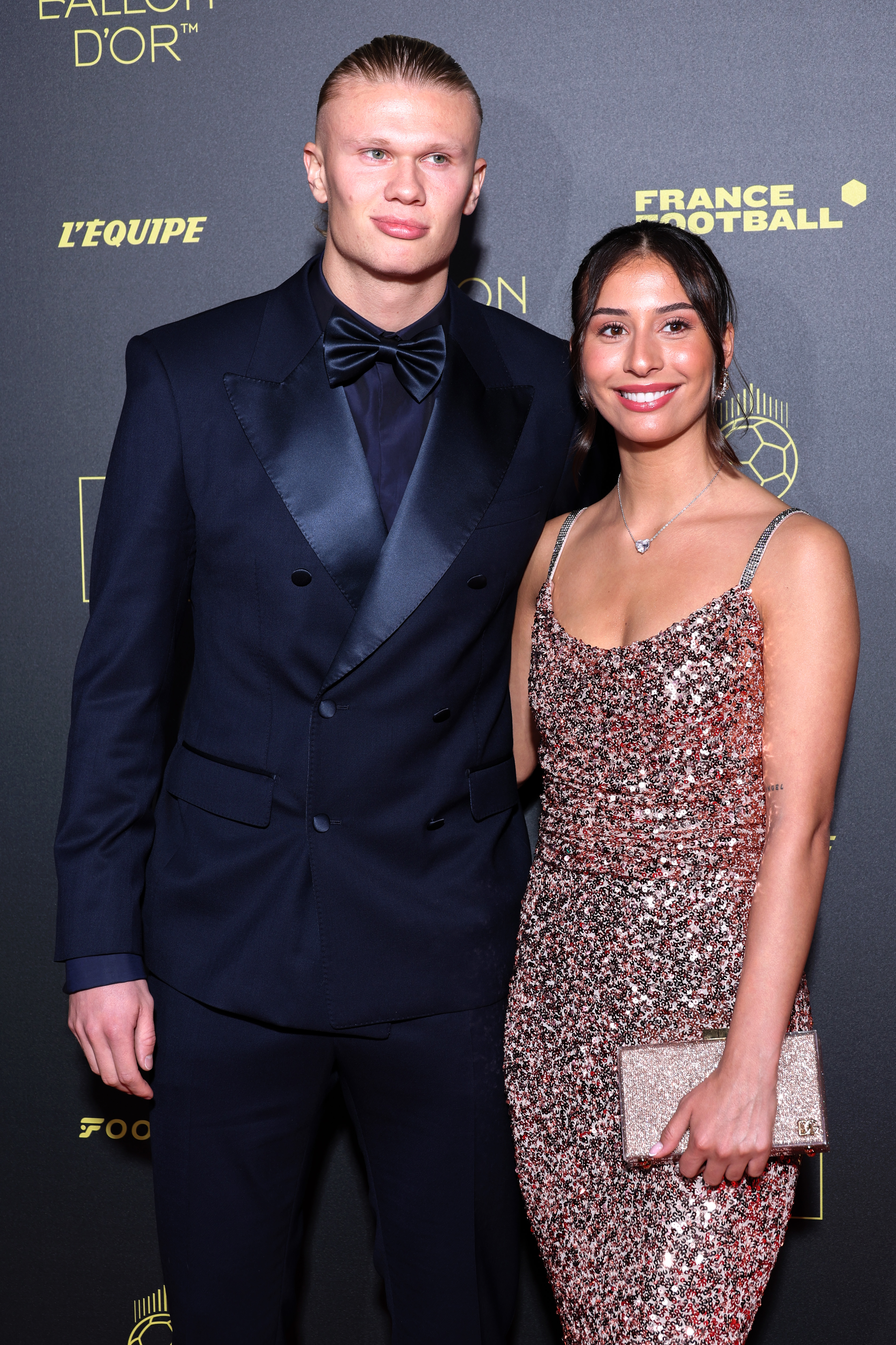 Erling Haaland in a navy tuxedo and Isabel Haugseng Johansen in a sparkly pink dress posing at the Ballon D'Or photocall in Paris.