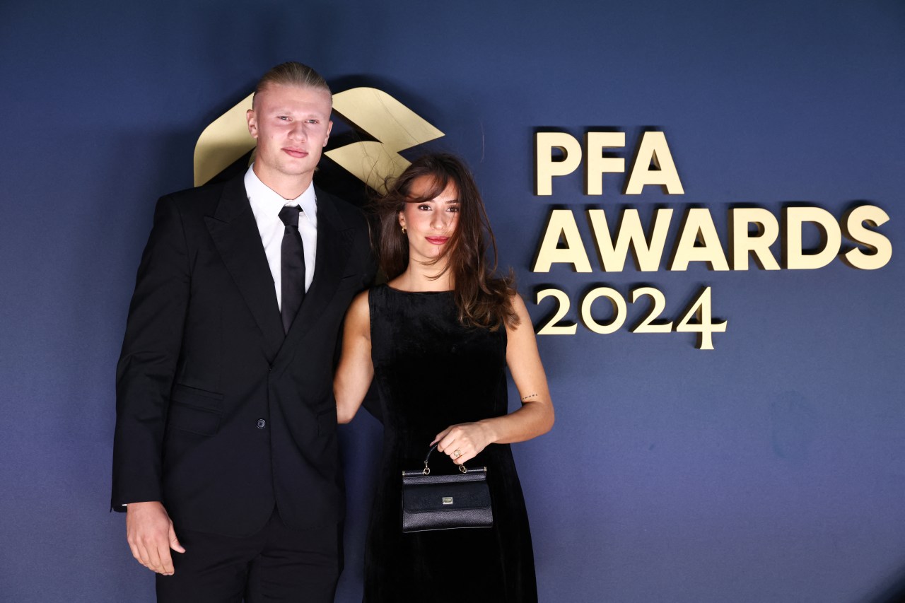 Erling Haaland in a black suit and Isabel Haugseng Johansen in a black dress posing in front of the PFA Awards 2024 backdrop.