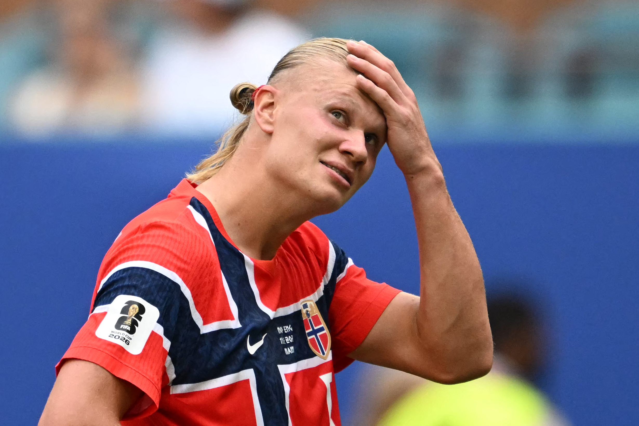 Erling Haaland in Norway's red kit holds his hand to his forehead with a pained expression during a match.