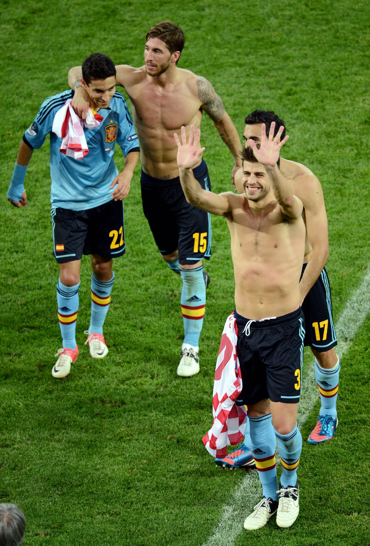 Shirtless Spain players celebrating on the pitch after a Euro 2012 match, with the No. 3 player waving to the crowd.