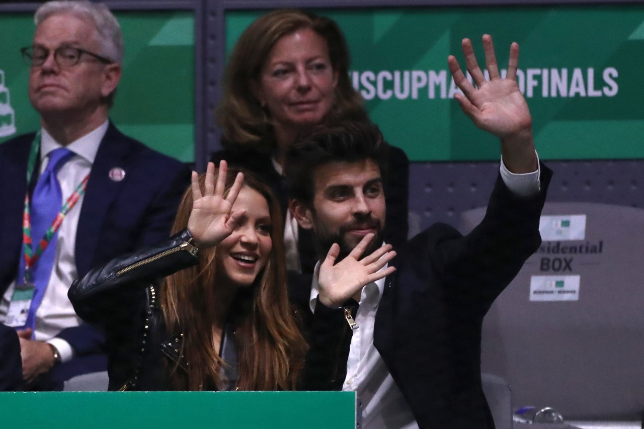 Shakira and Gerard Piqué smiling and waving from the stands at the 2019 Davis Cup Finals in Madrid.