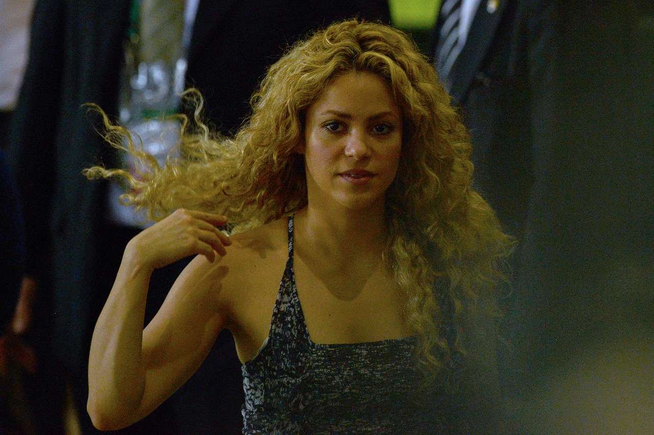 Close-up of a curly-haired woman in a dark tank top at a football stadium, her hair blowing to one side.
