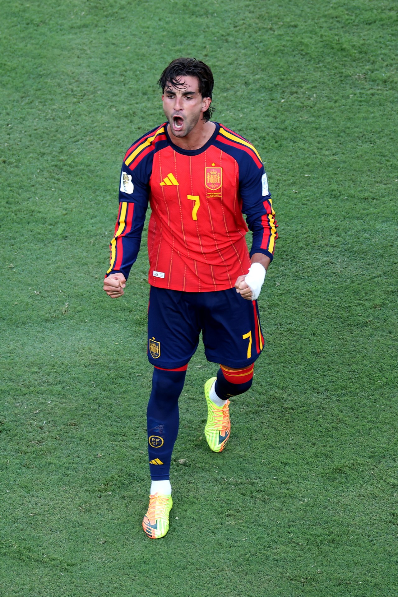 Ferran Torres in Spain's red number 7 jersey celebrates with fists clenched and mouth open on a football pitch.