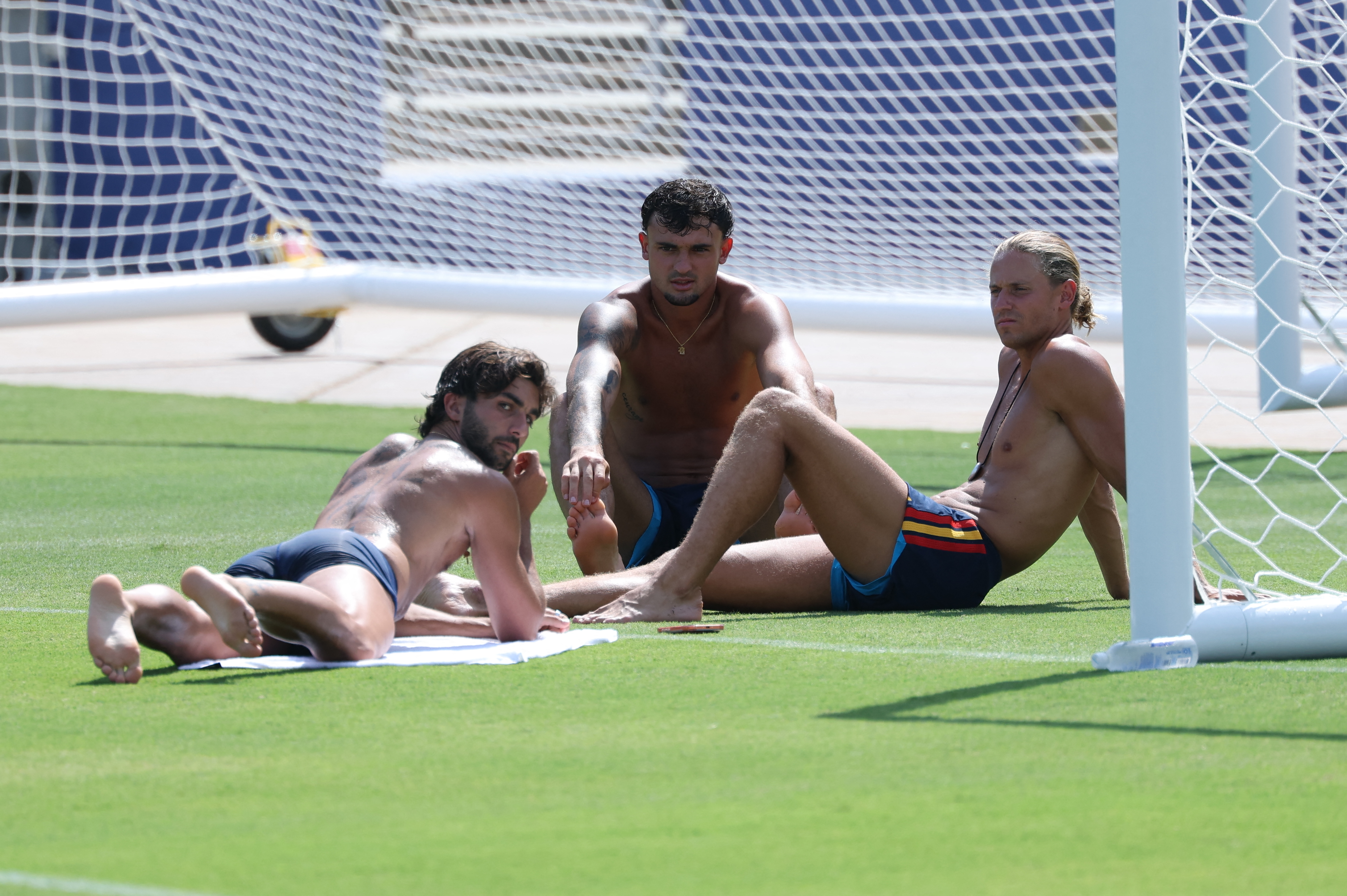 Ferran Torres, Marc Pubill, and Marcos Llorente sitting in the sun at a Spain training session at the Cotton Bowl in Dallas