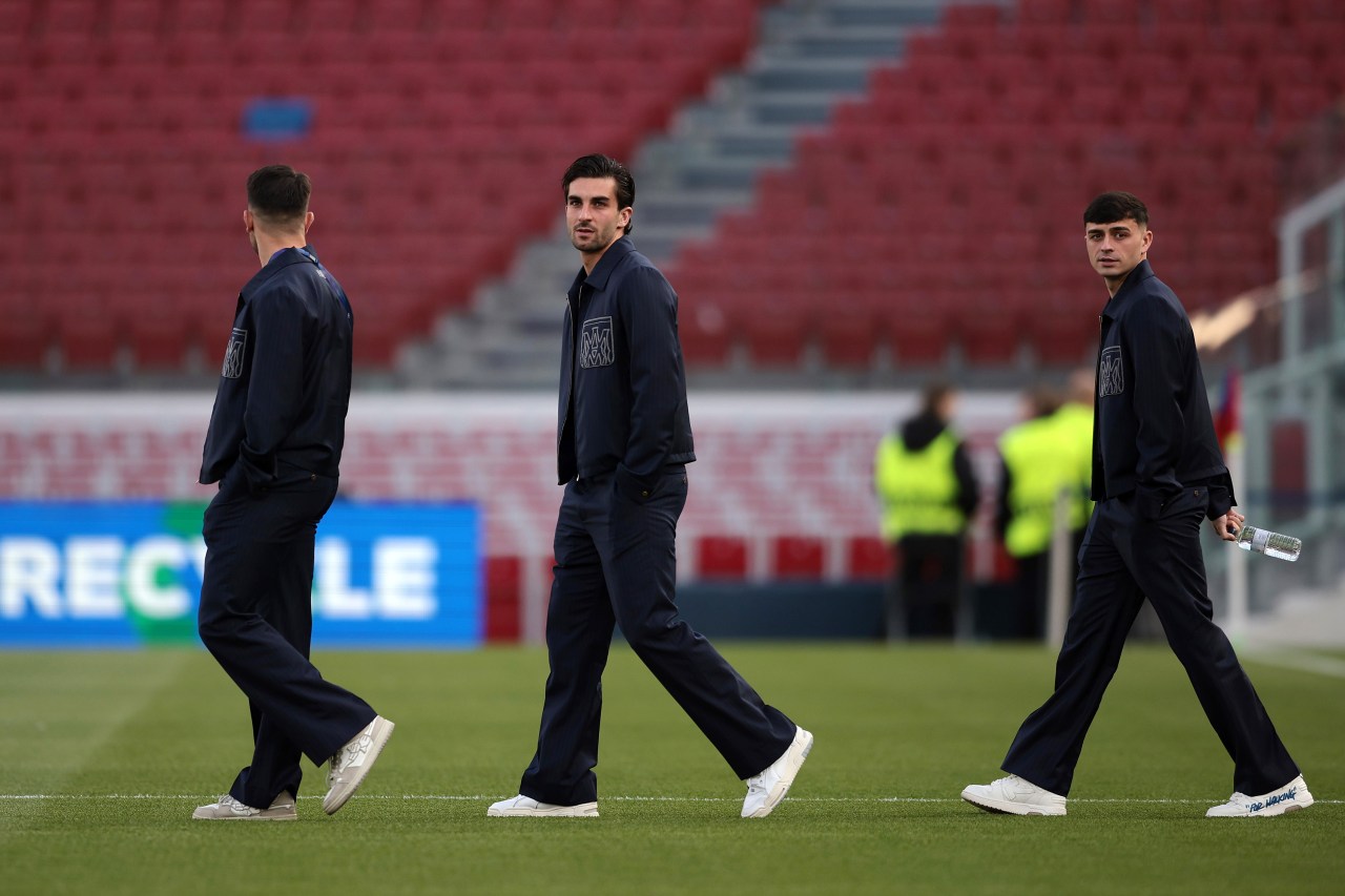 Three FC Barcelona players in matching navy tracksuits walking across the pitch inside Camp Nou stadium before a match.