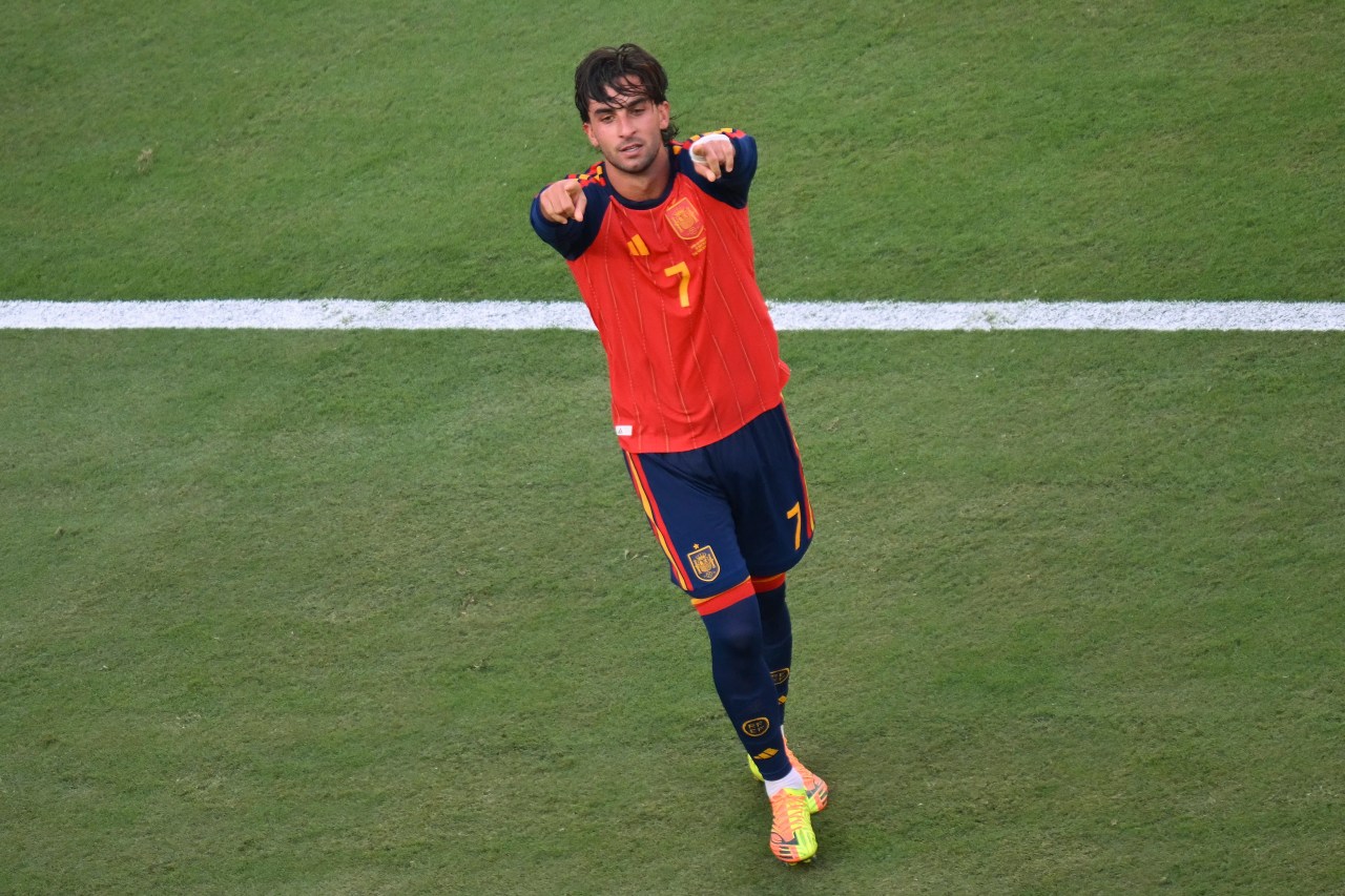 Ferran Torres in Spain's red and navy number 7 kit pointing both fingers toward the camera on a football pitch.
