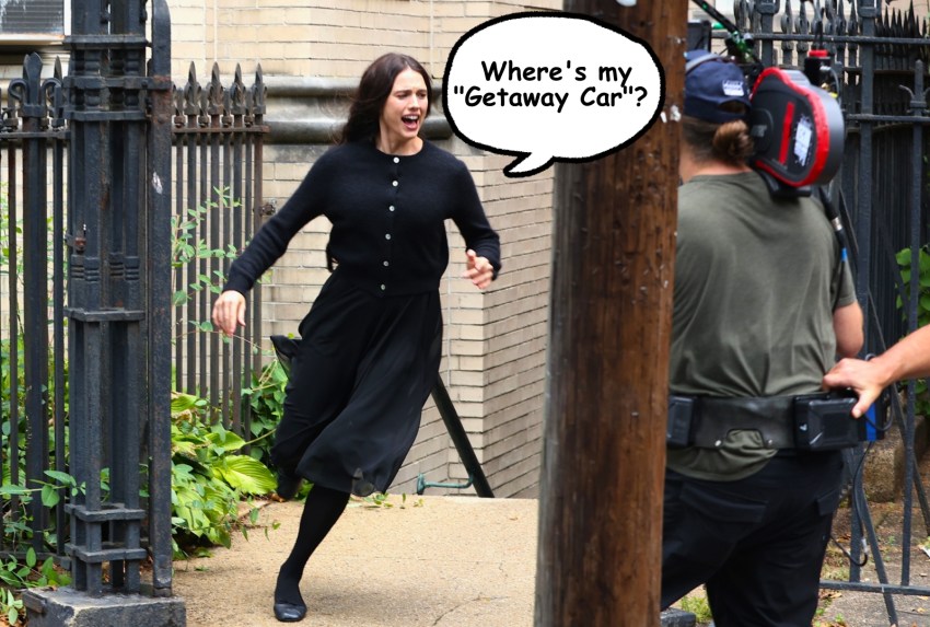 Actress in a black cardigan and skirt runs along a sidewalk near an iron fence while a camera operator films her on a city street.