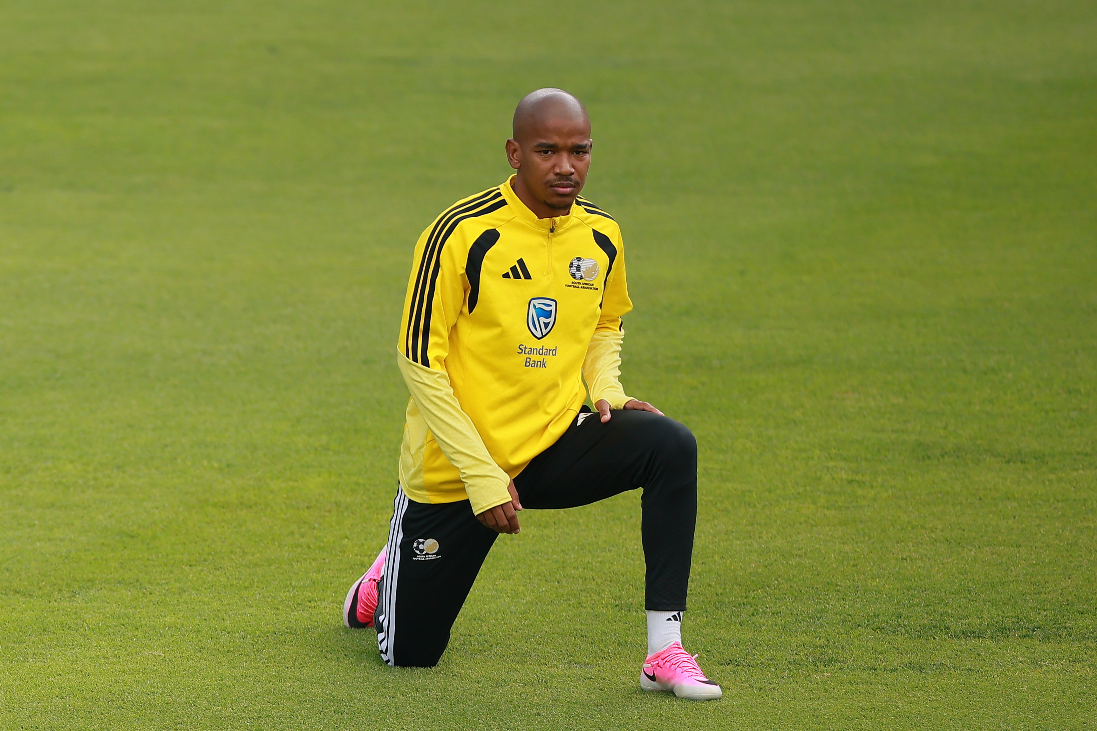 Jayden Adams in a yellow South Africa Adidas training jacket kneeling on one knee on a grass pitch, looking directly at the camera.