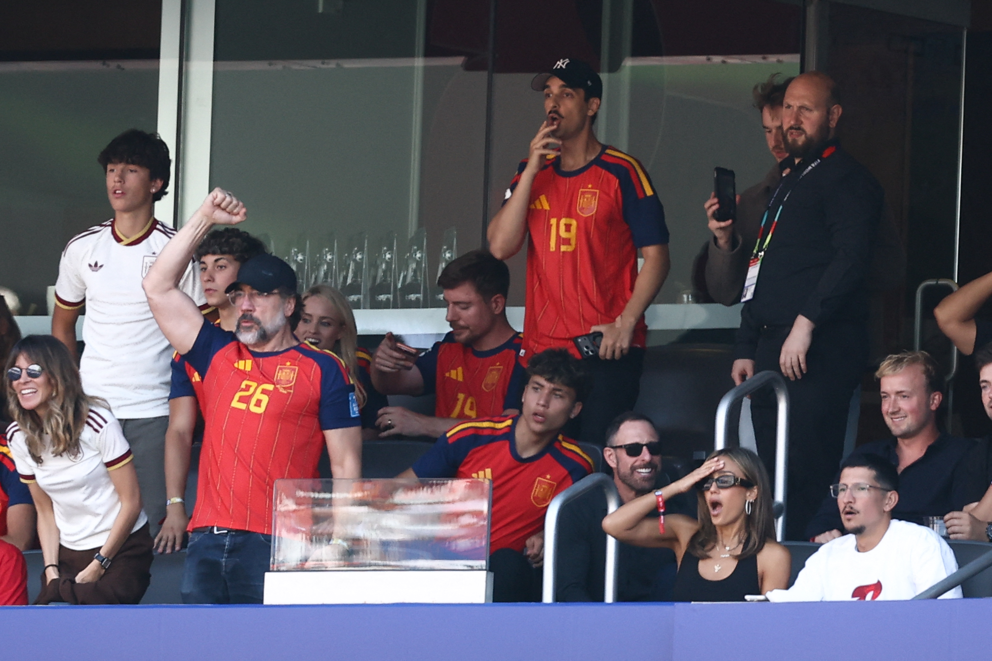 Jessica Alba, Danny Ramirez, and Javier Bardem reacting in the stadium stands at the 2026 World Cup final