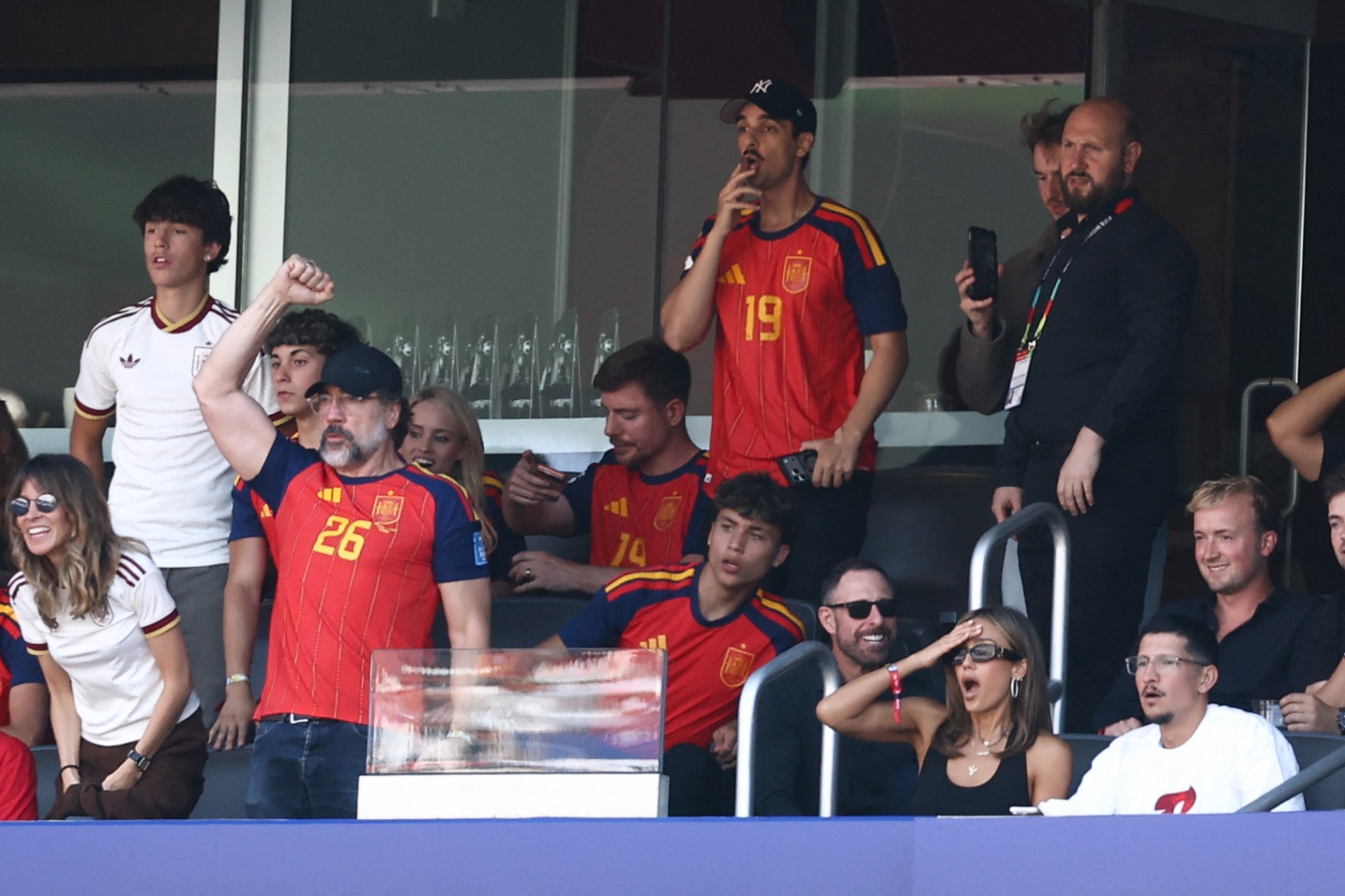 Jessica Alba, Danny Ramirez, and Javier Bardem reacting in the stadium stands at the 2026 World Cup final