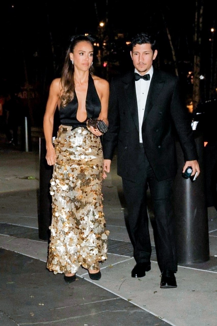 Woman in black halter top and gold sequin skirt walks alongside a man in a black tuxedo on a sidewalk at night.