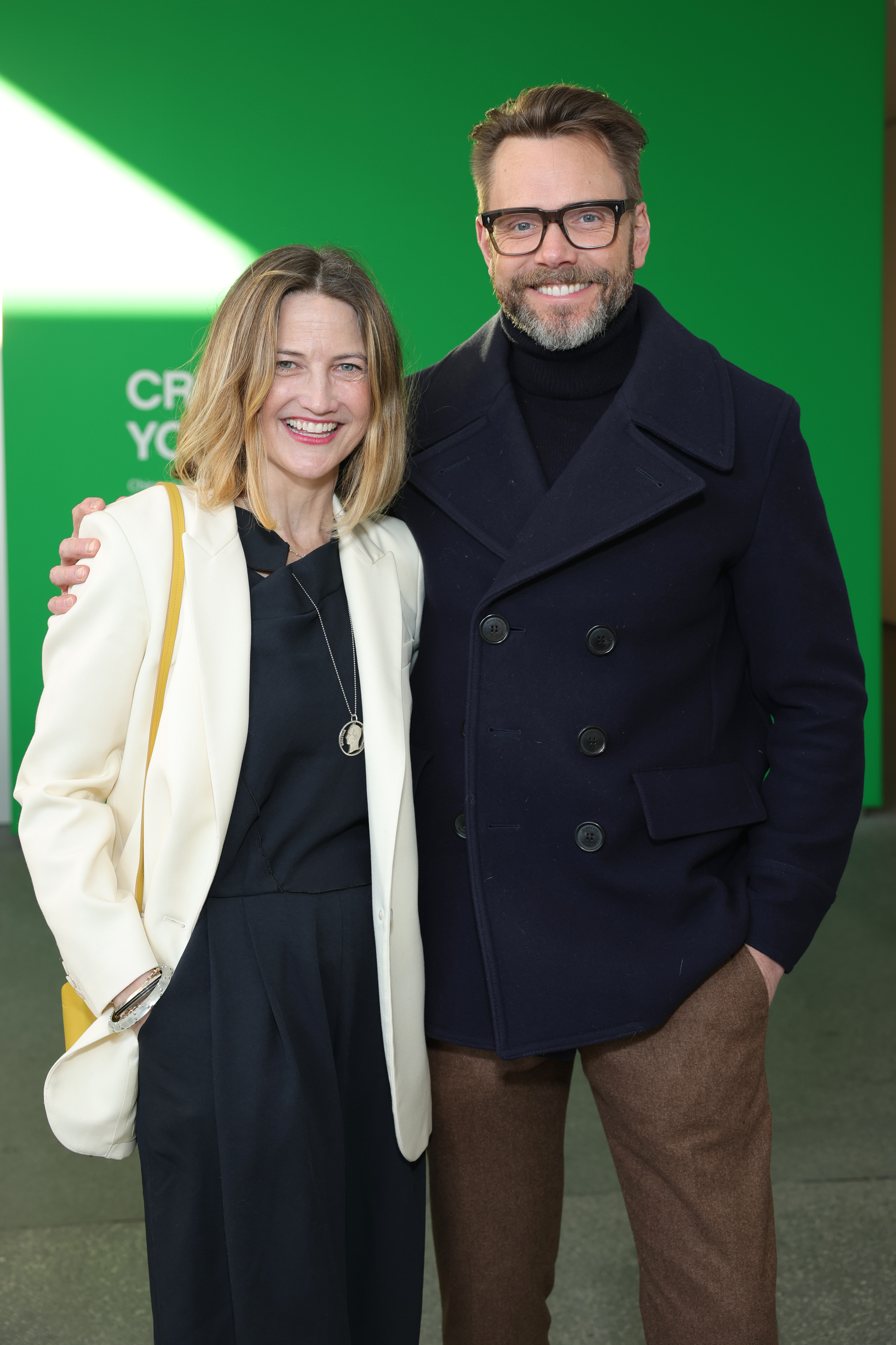 Sarah Williams and Joel McHale smiling together in front of a green backdrop at the Hammer Museum event.