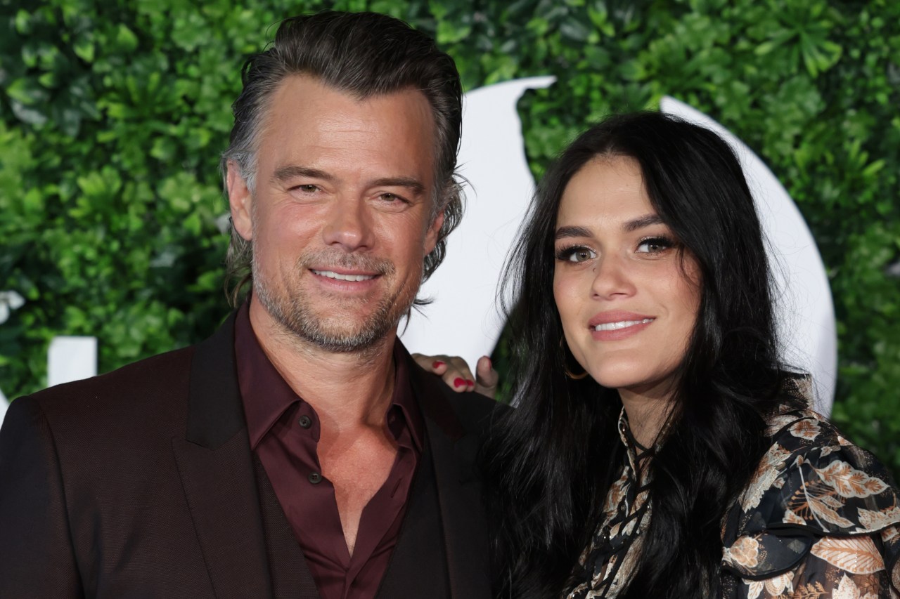 Josh Duhamel and Audra Mari smiling together in front of a green leafy backdrop at the Monte Carlo TV Festival.