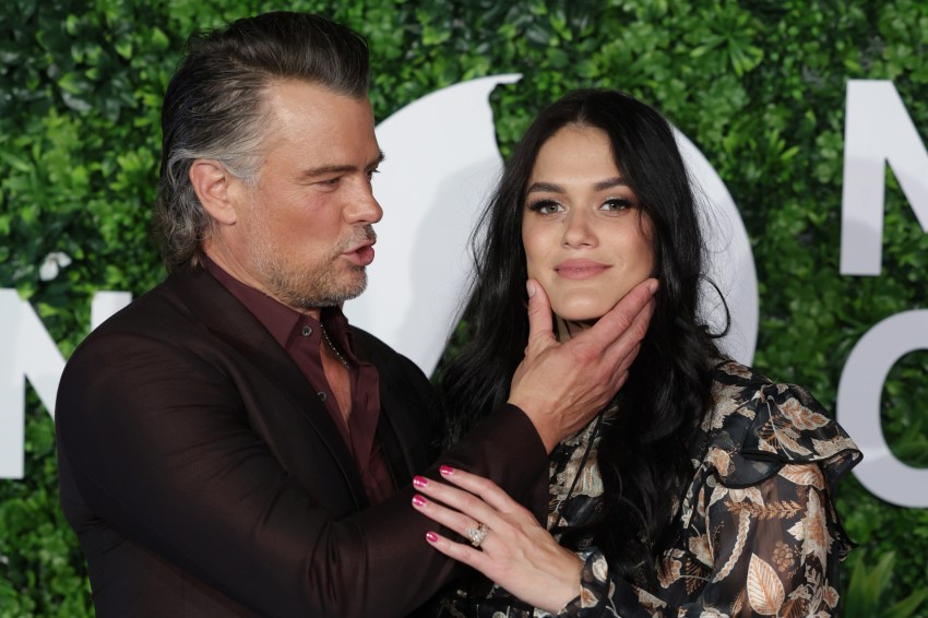 Josh Duhamel in all black and a pregnant Audra Mari in a floral dress pose at the Preschool screening step-and-repeat in Los Angeles.