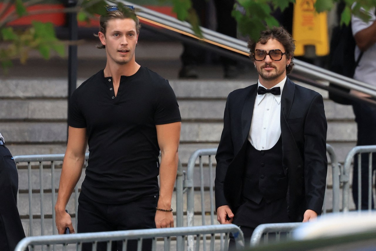 Two men walking outside Madison Square Garden — one in a black t-shirt with sunglasses on his head, the other in a black tuxedo with large sunglasses.