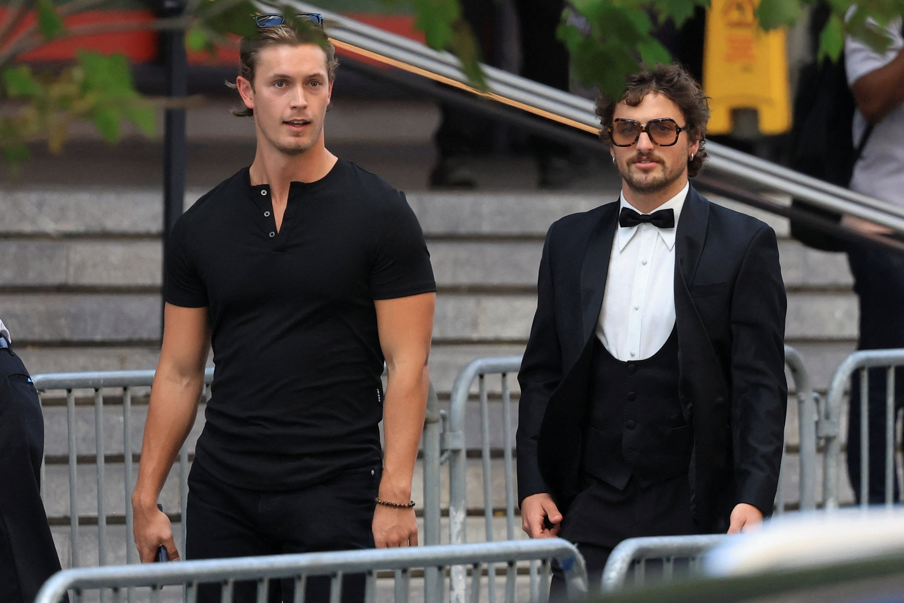 Two men walking outside Madison Square Garden — one in a black t-shirt with sunglasses on his head, the other in a black tuxedo with large sunglasses.
